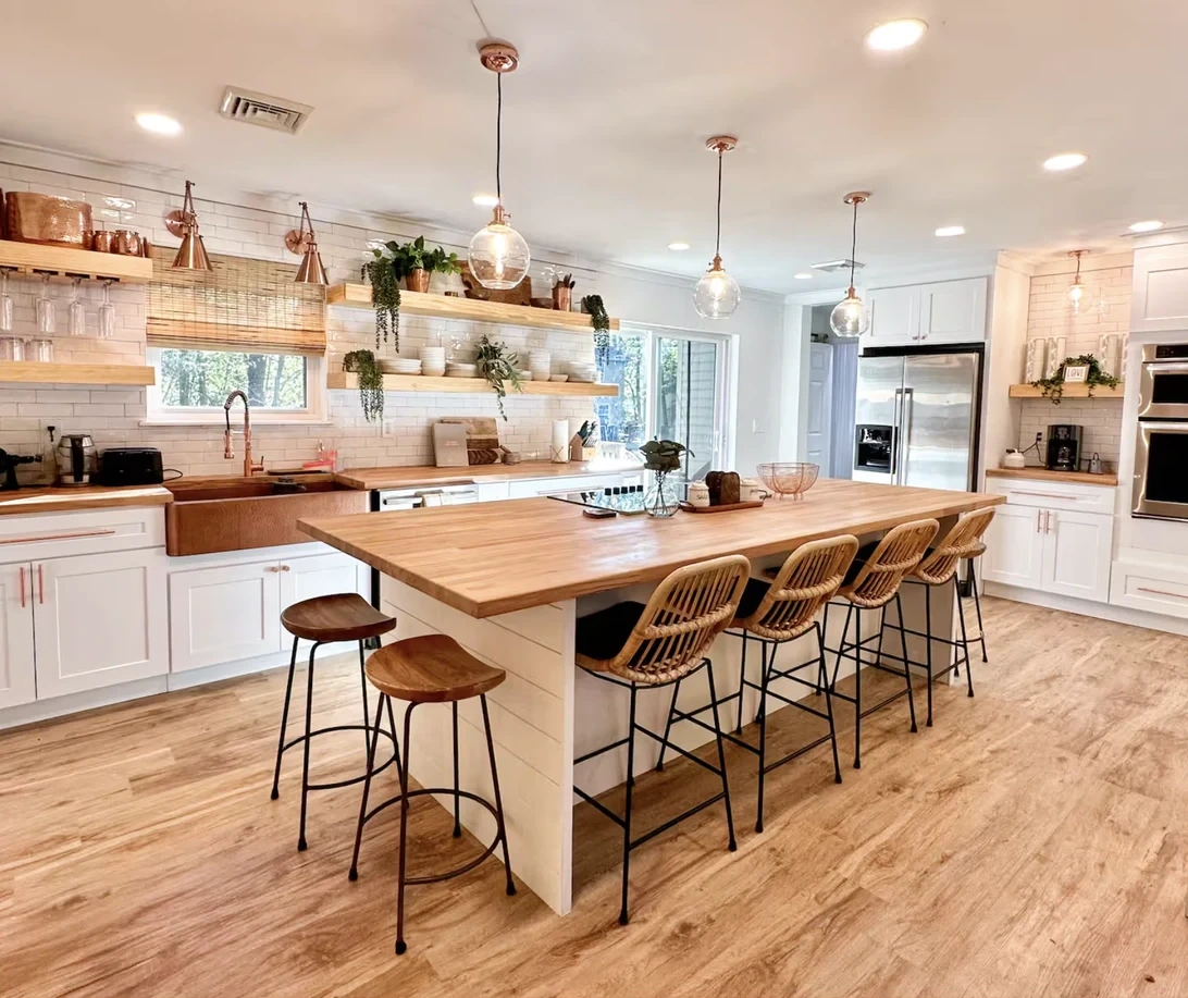 Renovated kitchen with a long butcher-block island, bar stools, white cabinets and open wood shelving