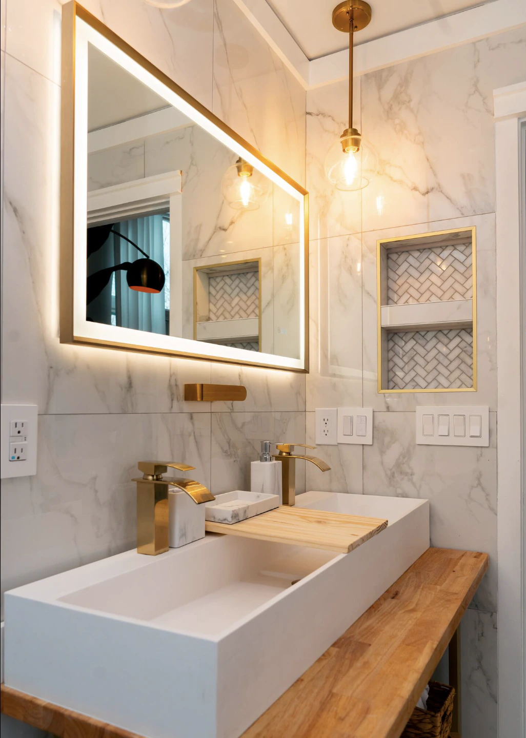 Primary bathroom with marble-look tile, a lit mirror and gold fixtures