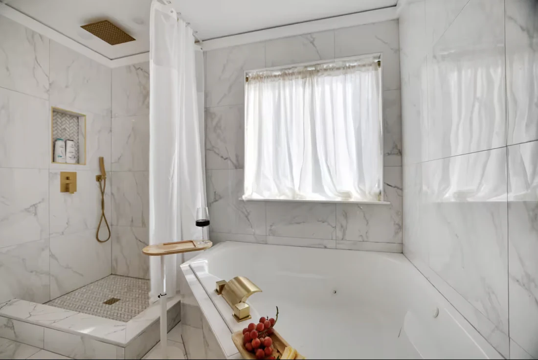 Tub set in marble-look tile with a gold faucet and a window above
