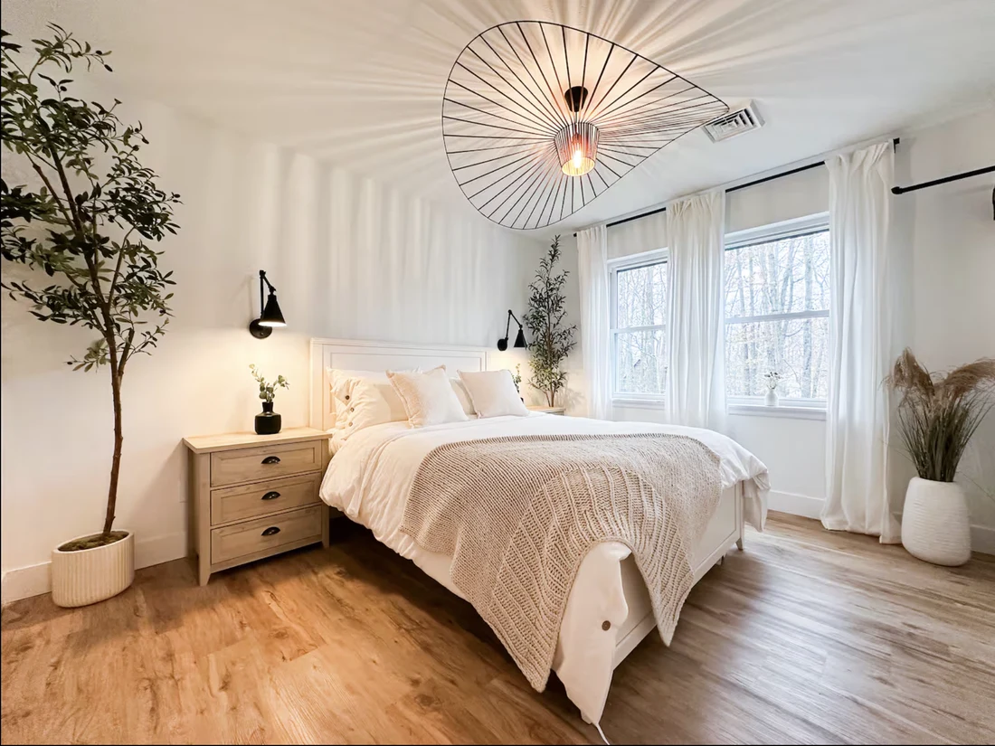 Bright bedroom with light wood floors, a woven pendant light and white walls